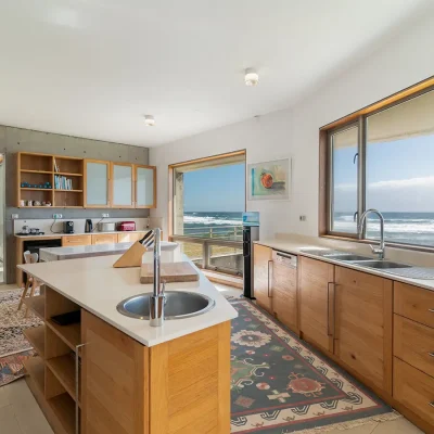 Modern kitchen in Villa De L'Ocean with wooden cabinets, and an angular kitchen island, with decorative floor carpets and large wooden frame windows looking onto the ocean.