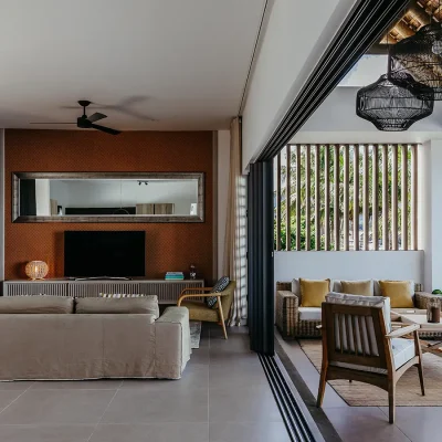 Open plan lounge with soft beige sofa facing a burnt orange wall with a television cabinet and narrow mirror that expands onto the terrace with additional outdoor seating via large sliding doors. Black River Penthouse.