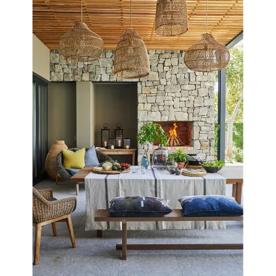 Covered outdoor dining table with woven hanging lights, and a stone wall with a built in fireplace.