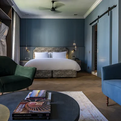 Bedroom suite painted in soothing shades of blue, with accents of colour in the velvet green armchair and blue velvet sofa, and the luxurious bed with crisp white linen, and glamour in the ceramics and lighting. Labotessa hotel.