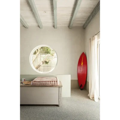 Room in pebbles with a wooden cabinet, a red surf board, and a large circular window.