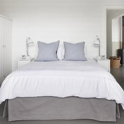 Cosy bedroom with white cladded walls that match the built in cupboards and desk, charcoal epoxy flooring and a spacious bed with crisp white linen and two white side tables.