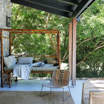 Outdoor bamboo four poster sun bed with decorative pillows positioned against Pinebeach verandah stone wall.