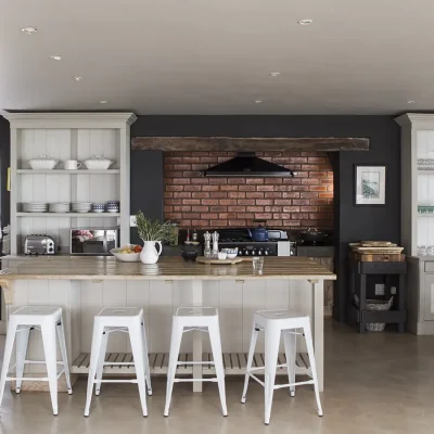 Quaint beach house Zonnestraal kitchen with a charcoal finish, large gas stove and oven, white wall cabinets and a central kitchen island with white cabinets and wooden counter tops paired with white bar stools.