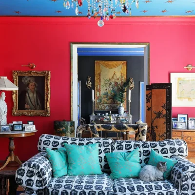 A lounge full of art, with bright red walls, a blue ceiling with gold stars and furnished with a black and white sofa with blue scatter pillows, wooden cabinets and a variety of wall art. Villa Toscana.