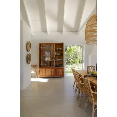 Open plan dining space with beige epoxy flooring and white walls, and a wooden dining table that compliments the large wooden framed glass cabinet. Buchubos Villa.