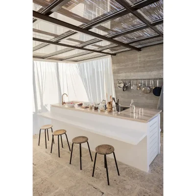 Casa Piana kitchen with a white marble island and extended bar top with wooden bar stools facing a stonewashed wall with hanging pots.