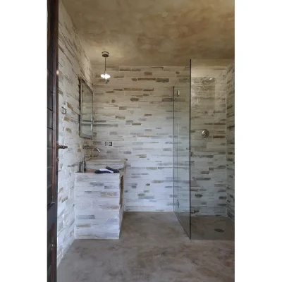 Bathroom with layered grey stone walls, an enclosed glass shower, and a large stone sink with a mounted mirror on the wall. Villa Sunshine.