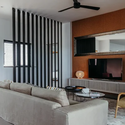 Soft beige sofa that reflects through the rugs and the walls, and facing a burnt orange wall with a television cabinet and narrow mirror. Black River Penthouse.