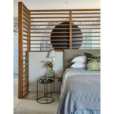 Open plan contemporary bedroom with grey hues bedding, stacked side tables and an en-suite bathroom separated by wooden wall frame.