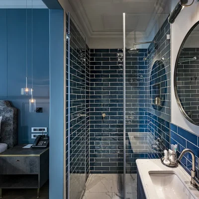 Labotessa Hotel en suite bathroom with a singular washbasin and mirror, a glass enclosed shower with deep blue wall tiling that compliments the bedroom shades of blue on the wall and bed.