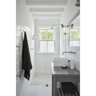 Bathroom with white cladded walls, a ceramic washbasin, and a glass enclosed shower with stone flooring and a window. Noordhoek Beach House.