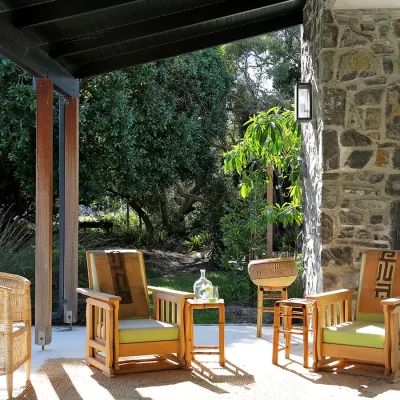 Protected Pinebeach verandah with cushioned wooden armchairs and a woven chair overlooking the luscious garden.