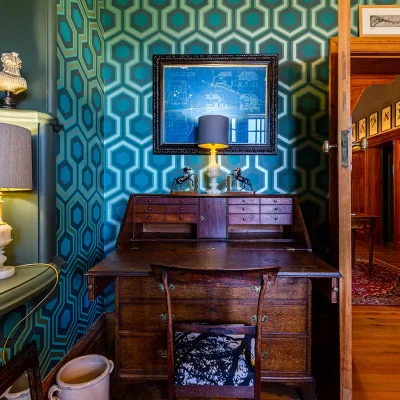 Wooden English Writing Bureau with blue green honeycomb wallpaper and framed architectural plans. House Nouveau.