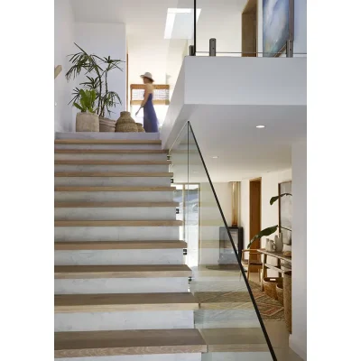 Staircase with marble and wooden stairs and a glass railing revealing the free standing fire place on the first floor of Walkers Beach Villa.