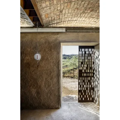 A cellar room with original clay and lime walls that reflect in the floor, a brick arched ceiling and a rusted door with slits that opens onto Karoo vegetation.