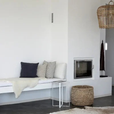 Whitewashed walls and epoxy floors with an indoor Austrian-style fireplace and neighbouring white bench decorated with white furs and scatter pillows. Feng Shui.