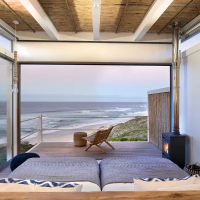 Sunset from Lekkerwater Beach Lodge bedroom suite with joint twin beds, a free standing fireplace and large glass windows and stack back doors that open onto the deck with panoramic views of the coast.