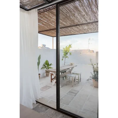 Outdoor terrace with whitewashed walls and stone floors, and a bamboo pergola protecting the rustic wooden table and chairs. Casa Piana.