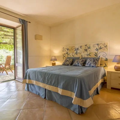 Light and airy suite in Villa Sunshine with cream textured walls and double doors that open onto the outdoor terrace, and furnished with a spacious bed with blue linen and two bed side tables with lamps.