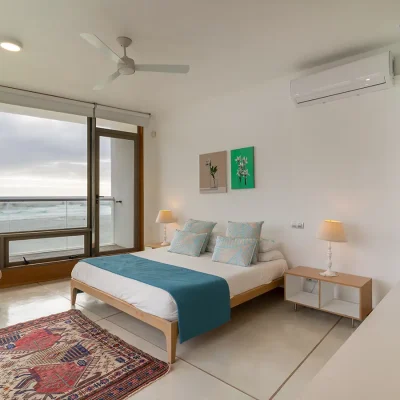 Private bedroom in Villa De L'Ocean with double bed, floating bookshelves, an armchair and wall air conditioner, with large windows and a door that opens onto the deck with surrounding sea views.