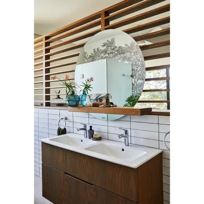 En-suite bathroom with double sink and a large circular mirror backed on a contemporary wooden wall frame.