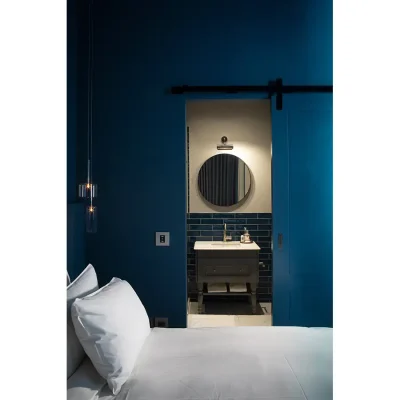 Bedroom suite in Labotessa Hotel with deep blue walls that match the wooden sliding door that reveals the ensuite bathroom with a ceramic washbasin and circular mirror.