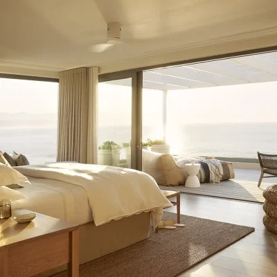 Walkers Beach Villa bedroom suite with luxurious white linen bed, wooden coffee tables and surrounded by large glass stack doors that open onto a private patio with ocean views.