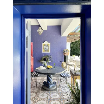 Protected outdoor patio with decorative tiling and deep blue walls with a circular granite table and heart shaped metal chairs. Villa Toscana.