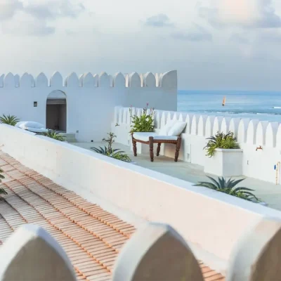 The rooftop relaxation area with hints of Arabic architecture reflected in the cropped whitewashed walls, wooden benches with white pillows and plant boxes.