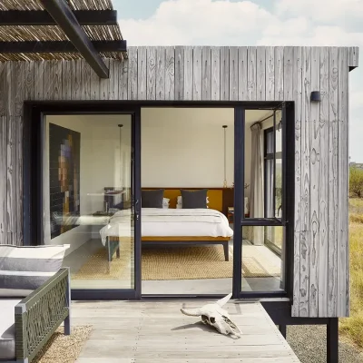 Contemporary bedroom suite with a spacious wooden bed decorated with crisp white linen and opening onto the wooden patio via large glass sliding doors. The Herenberg.