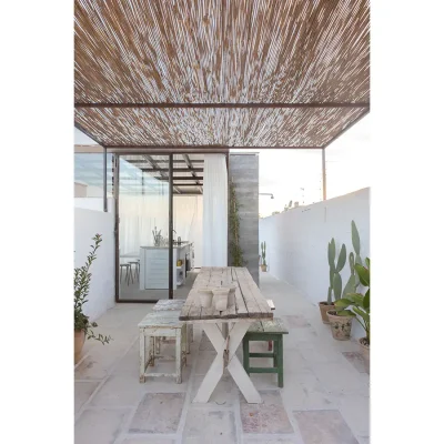 Glass sliding doors that open Casa Piana kitchen onto the outdoor terrace. with a rustic wooden table and chairs protected by a bamboo pergola.