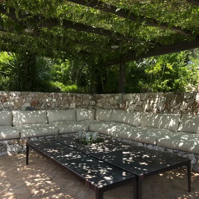 Outdoor lounging area with a built in stone corner couch and spacious drinks table that is shaded by a large pergola wrapped in vine leaves. Villa Sunshine.