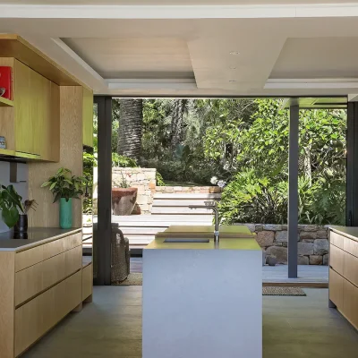 Modern kitchen with sleek wooden cabinets and a central kitchen island that opens onto views of the back garden via large stack back doors. Oasis On glen.