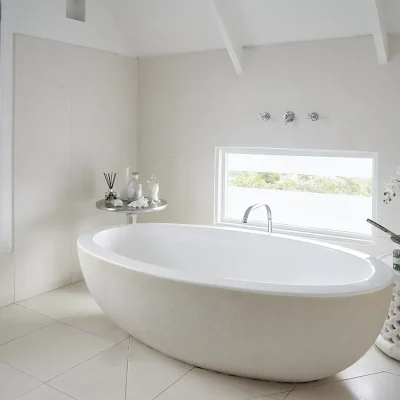 Bathroom in Noordhoek Beach House with a free standing white oval shaped bath with views of the garden through a lengthy window.