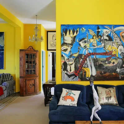 Lounge with bright yellow walls decorated with large abstract paintings, a navy blue sofa and a striped corner sofa with a Persian rug.