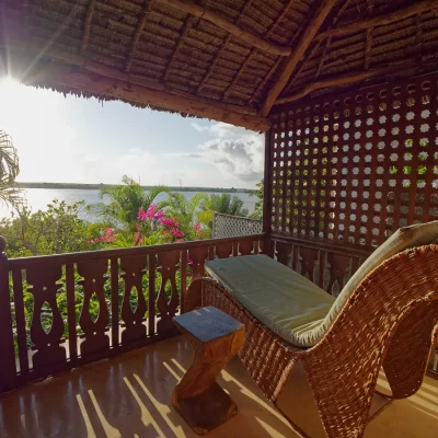 Balcony with a large wicker sun lounger and protected by a thatched roof, with views of the palm trees and shimmering ocean.