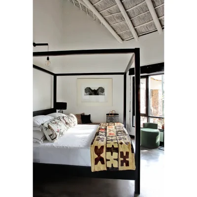 Spacious wooden four poster bed with white linen and decorative pillows and quilt in whitewashed Manor House bedroom with plentiful natural light from the large windows.