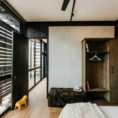 Bedroom suite with wooden cabinet, a leather ottoman, a beige linen bed and large glass windows with shutters. The View.