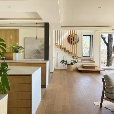 Open plan kitchen with sleek wooden cabinets and white granite tops that opens onto the dining and living area with wooden flooring and a contemporary staircase. Oasis on Glen.