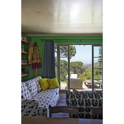 Lounge in Villa Toscana with black and white sofas on a red Persian rug facing green walls with large glass sliding doors revealing views of the city and distant mountain ranges.