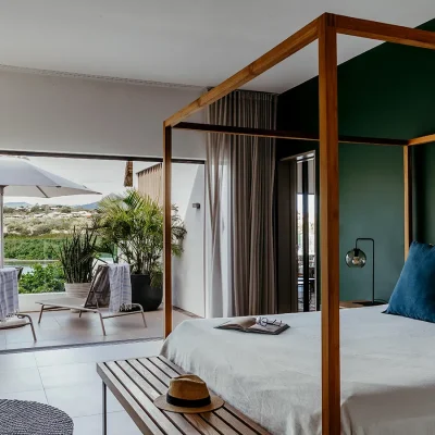 Four poster bed with white linen set against an emerald green wall opens onto Black River Penthouse Terrace and views of the mountain via large glass sliding doors.