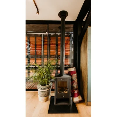 Free standing fireplace positioned next to a large pot plant and set in front of ceiling to floor glass stack back doors.