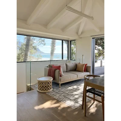 Oasis on Glen upstairs landing with a soft beige sofa positioned on a rug and a large glass window revealing the blue ocean as the backdrop.