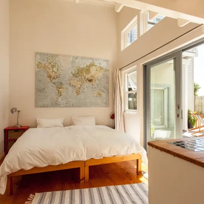 Large glass doors that open up Pebbles bedroom space, furnished with joined twin beds, crisp white linen, two side tables and a map of the world on the wall.