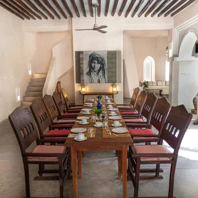 The Fort dining room with white washed walls, open archways and wall art, and furnished with a large wooden dining table and chairs.