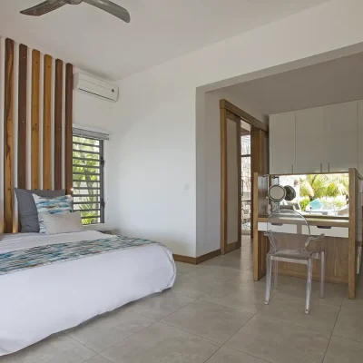 Light and spacious bedroom with a large bed set against a wooden panelled wall and contains an open plan closet and vanity table.