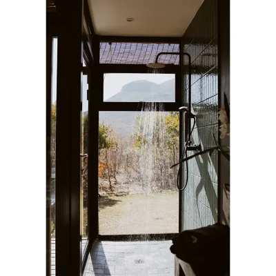 Open shower with a blue tiled wall and views of the bushveld from the ceiling to floor glass window. The Blogck.