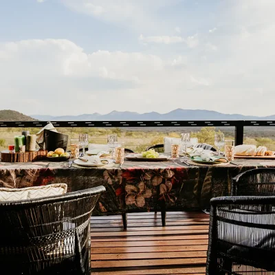 Outdoor dining table with black decorative table cloth and black wicker chairs overlooking the reserve and distant mountain ranges. The View.