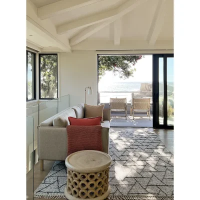 Oasis on Glen upstairs landing with a soft beige sofa positioned on a rug and large glass sliding doors opening onto a wooden deck with views of the ocean.